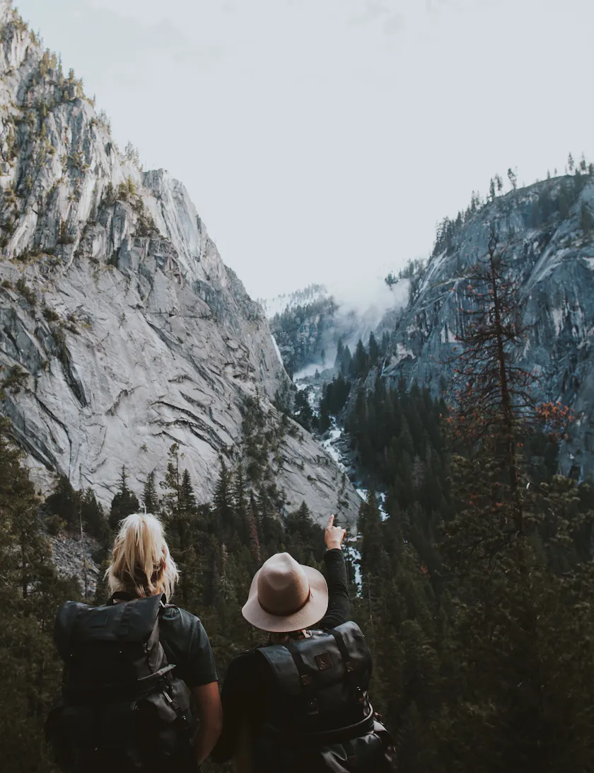Two hikers with backpacks looking out over a valley, one pointing at the view.